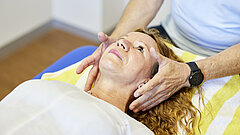 Eine Therapeutin hält ihre Hände neben den Kopf einer Patientin.
