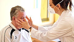 Eine Ärztin untersucht einen Patienten und hält beide Hände seitlich vor das Gesicht des Patienten.