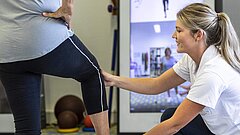 Eine Therapeutin unterstützt eine Patientin bei einer Übung und hält ihr Bein.