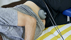 Am Bauch eines Patienten ist ein Gerät zur Muskelstimulation angeschlossen.