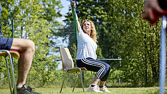 Eine Patientin absolviert im Sitzen im Freien eine Übung mit einem Terra-Band.