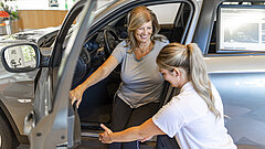 Eine Therapeutin unterstützt eine Patientin beim Aussteigen aus einem Auto.