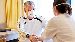 Eine Ärztin begrüßt einen Patienten mit einem Handschlag. Beide tragen einen Mund-Nasen Schutz.